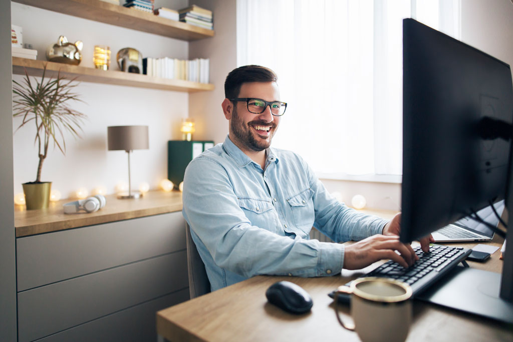 Lachender Mann an seinem Arbeitsplatz im Home Office.