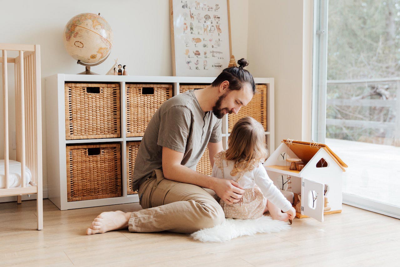 Un père joue avec sa petite fille avec une maison de poupées dans la chambre d'enfant.