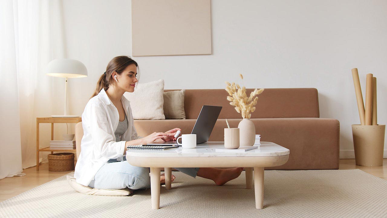 Vrouw zittend aan een woonkamertafel met haar laptop.