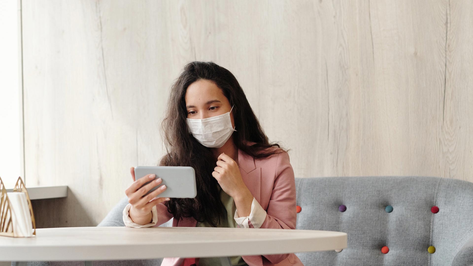 Frau mit Maske schaut auf ihr Smartphone.