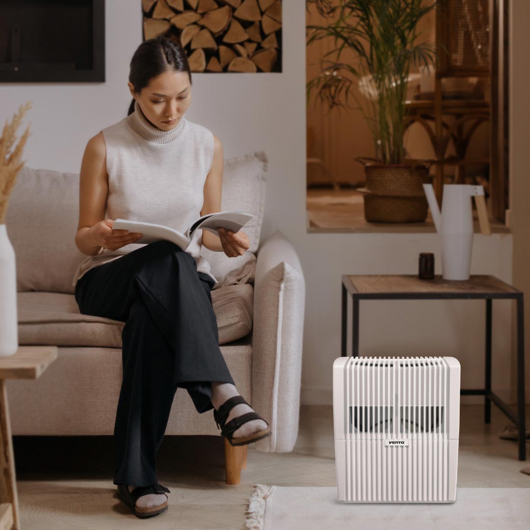 Madame lit un magazine dans le salon avec un humidificateur Venta pour créer un climat intérieur optimal.