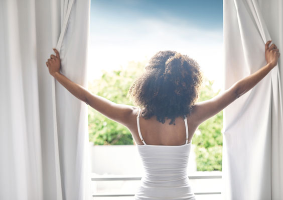 Frau öffnet nach dem Aufstehen die Vorhänge und sieht aus dem Fenster.