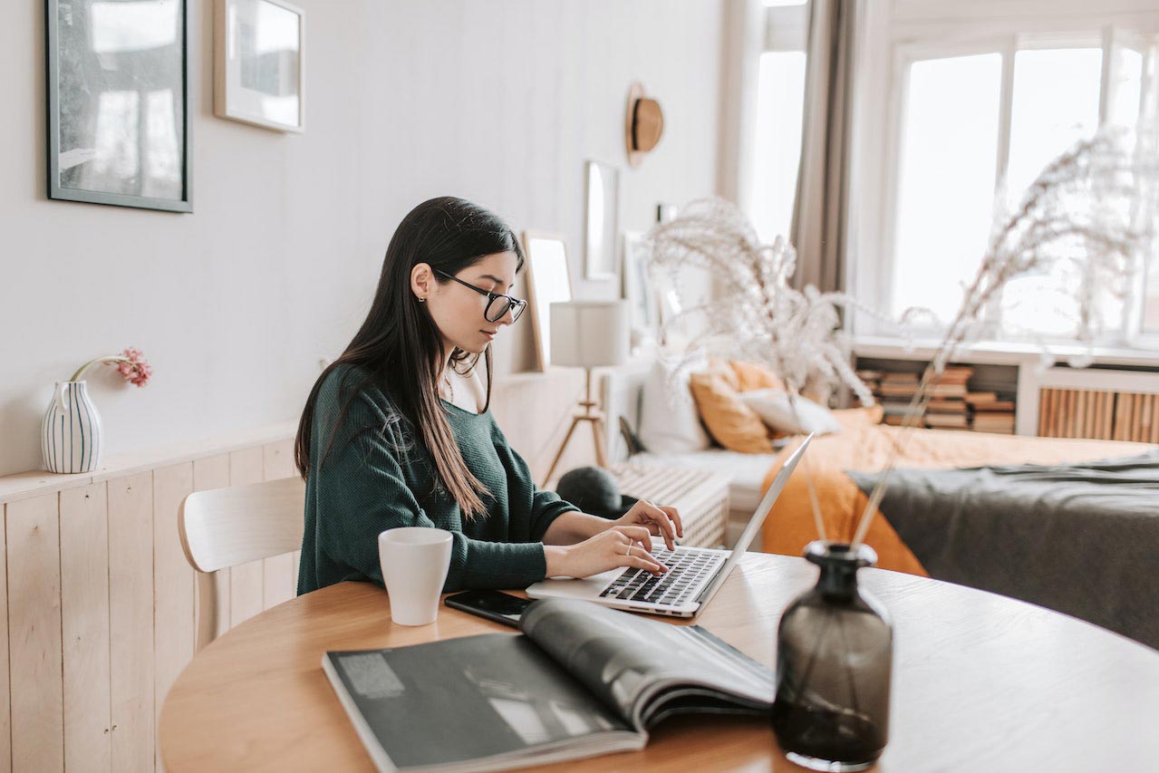 Woman sitting with her laptop at a wooden table in her living area.